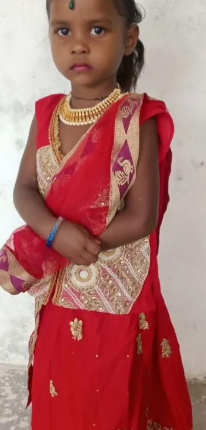 A child wearing a traditional red dress with gold designs and a matching headpiece.