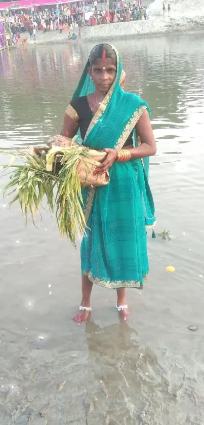 Woman in traditional attire performing ritual by a riverbank in vibrant setting.