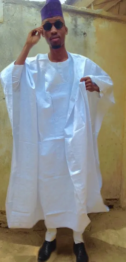 Person in traditional white attire outdoors with a wall backdrop.