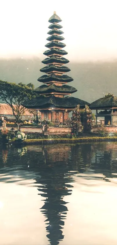 Bali temple reflects in calm lake under misty mountains.