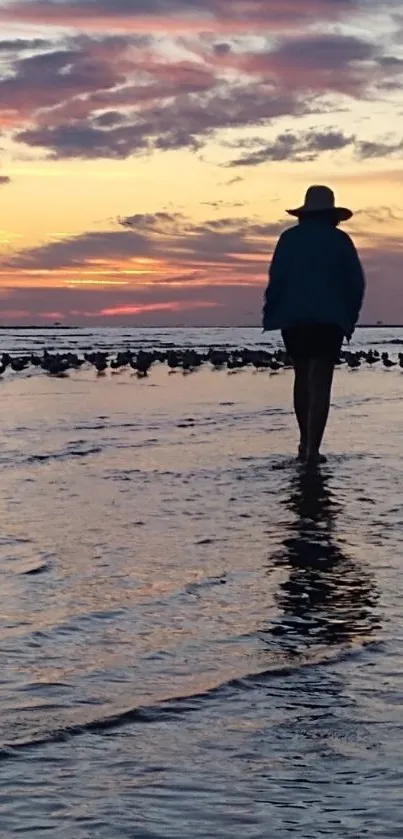 Silhouette of person walking on beach during vibrant sunset.