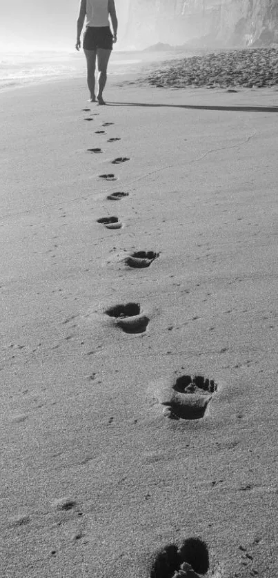 Monochrome beach walk with footprints leading to a distant figure.