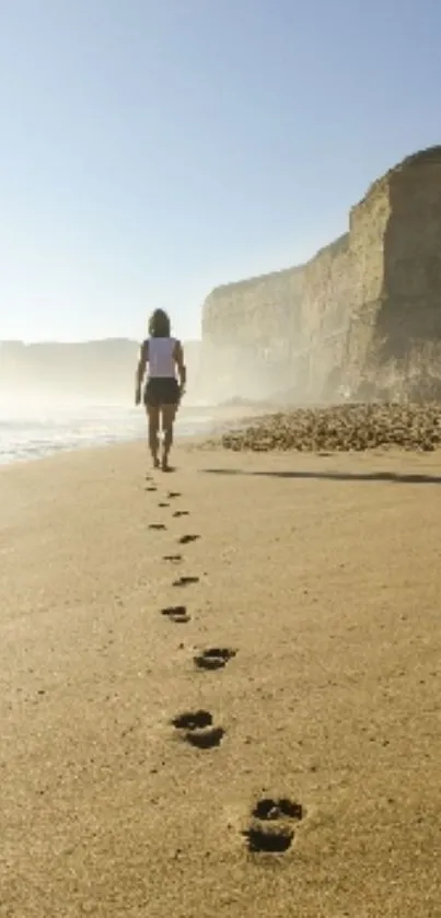 Person walking on sandy beach with cliffs in background.