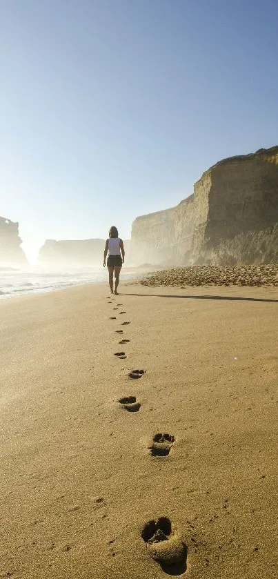 Footprints on a serene beach with woman walking along the shore at sunset