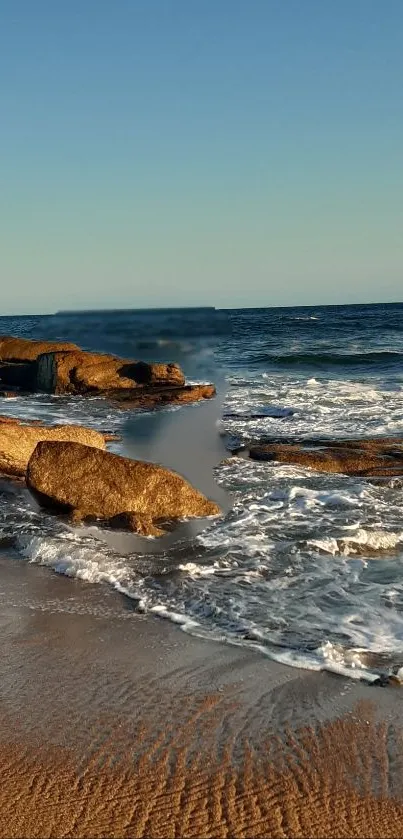 Calming beach scene with waves and rocks at sunset.