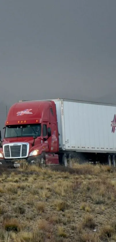 Red truck traveling through rugged terrain on a foggy highway.