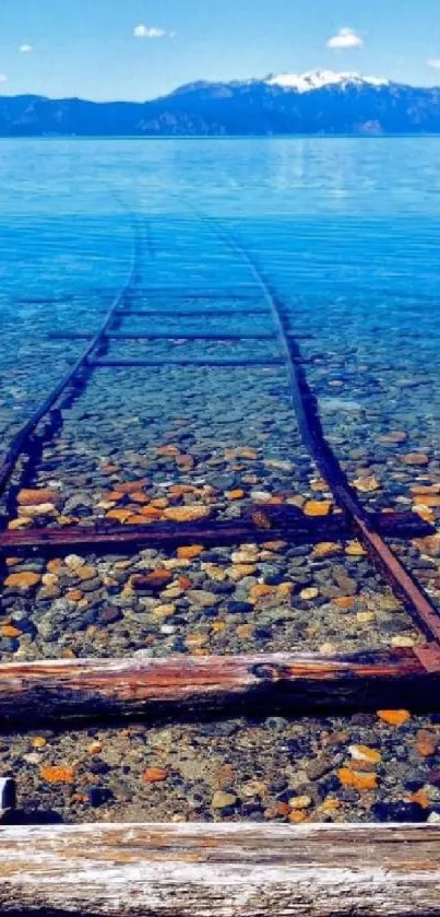 Rails leading into a clear blue lake with a mountain backdrop.