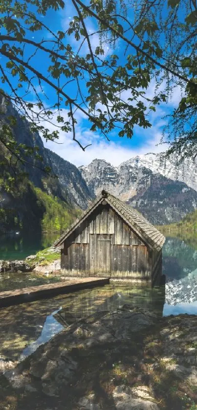 Scenic wallpaper of a cabin by a tranquil lake with mountains in the background.