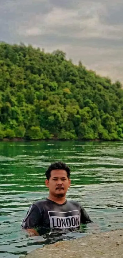 Man standing in a tranquil lake with lush green hills in the background.