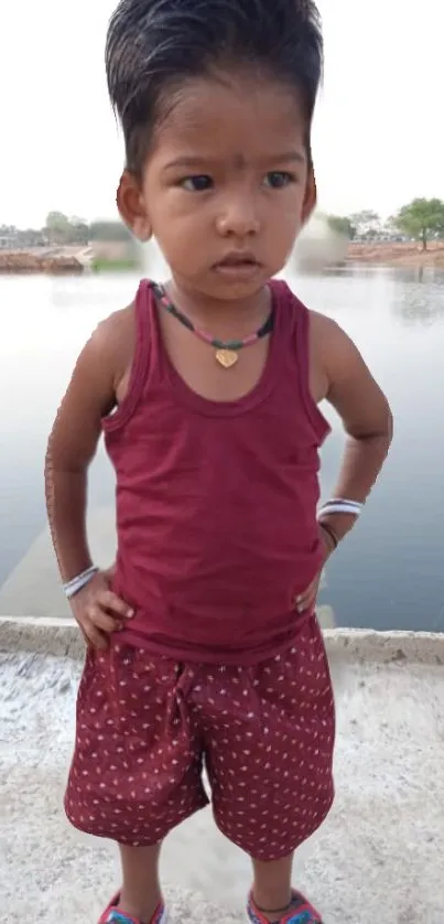 Young child in maroon attire by a serene lakeside.