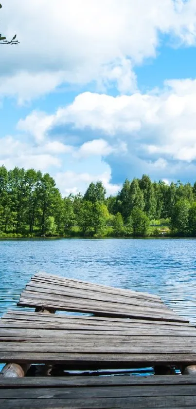 Rustic pier extending into blue lake with lush green forest under a bright sky.