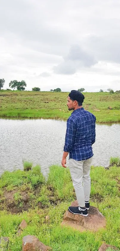 Man standing by a tranquil lakeside, surrounded by lush greenery.