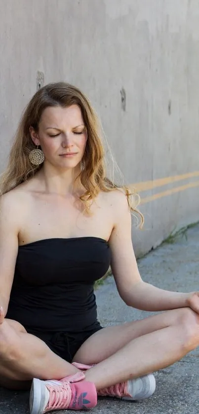 Woman meditating peacefully against urban wall in serene setting.