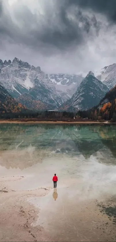 Person standing at calm mountain lake with cloudy sky.