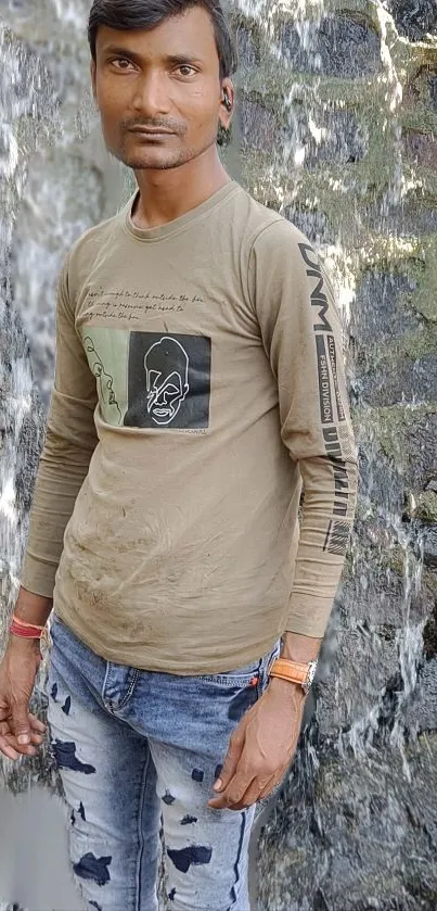 Man in casual attire standing by a serene waterfall.