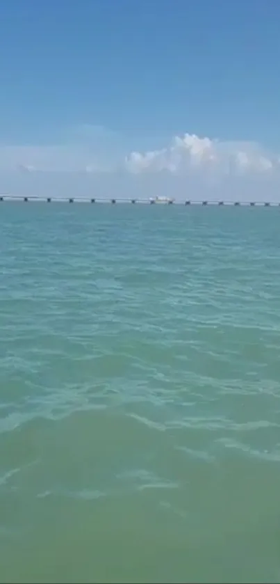 Calm ocean and distant bridge under a blue sky.