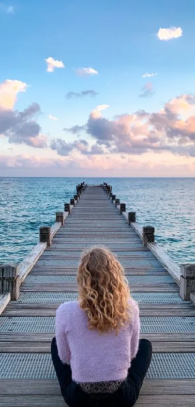 Woman sitting on pier gazing at ocean and sunset sky.