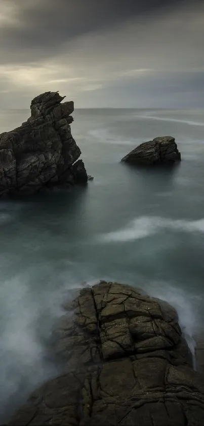 Serene ocean landscape with rocks and cloudy sky.