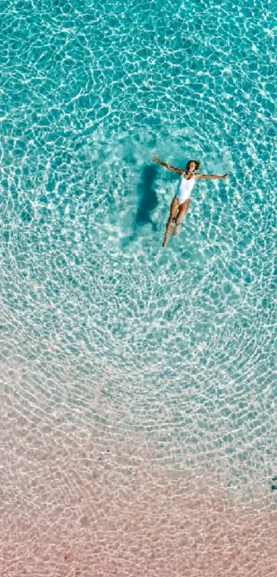 Aerial view of a person relaxing in turquoise ocean water near a pink sandy beach.