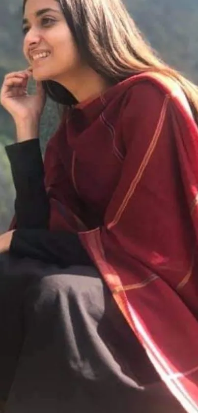 Woman in red shawl sitting outdoors with mountains in the background.