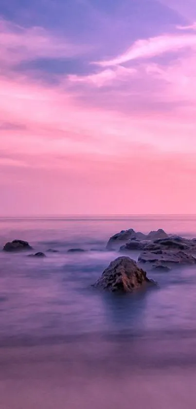 Dreamy pink sky over calm sea with rocks in foreground, creating serene wallpaper.