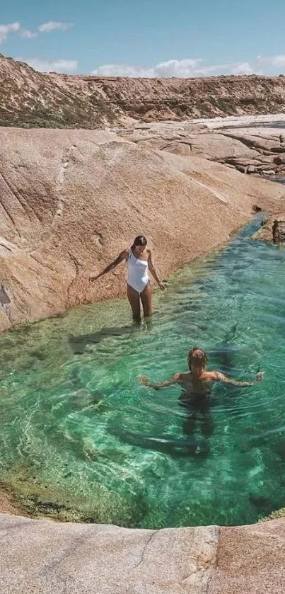 Two people enjoying a serene natural pool by the rocky coast.