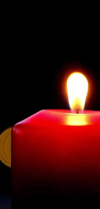 Red candle with glowing flame on black background.