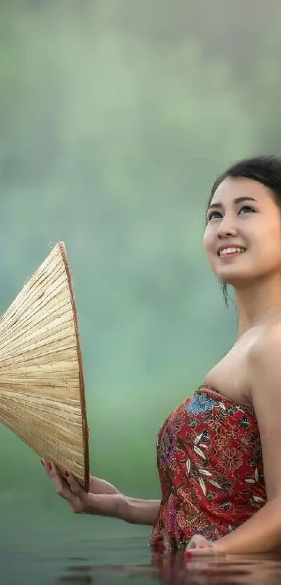 Peaceful woman in red dress holding a fan by a tranquil river.