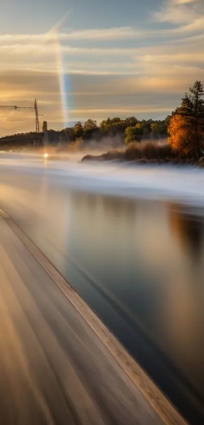 Sunset over tranquil river with autumn colors and distant rainbow.