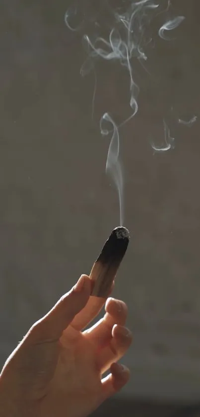 Hand holding a smoking stick on a dark background.