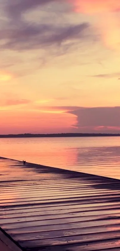 Sunset over calm lake with pink sky and wooden pier.