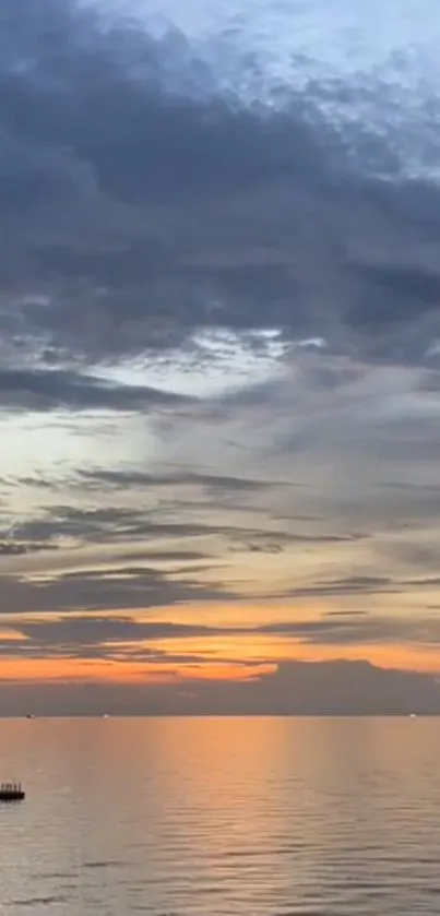 Sunset over ocean with orange sky and dark clouds.