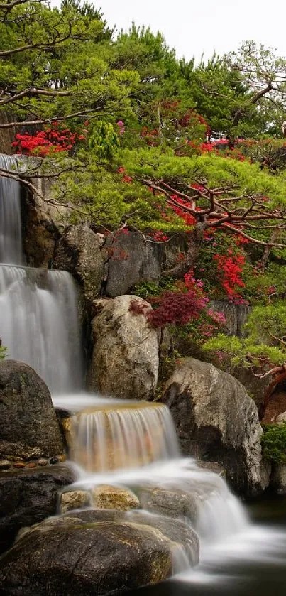 Soft waterfall flowing through a lush, green garden with vibrant red flowers.