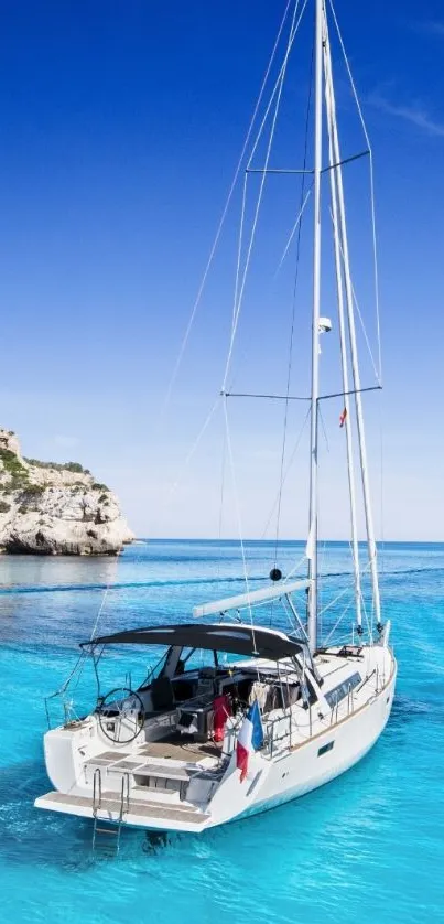 A yacht sailing on bright blue waters under a clear sky, with rocky cliffs nearby.