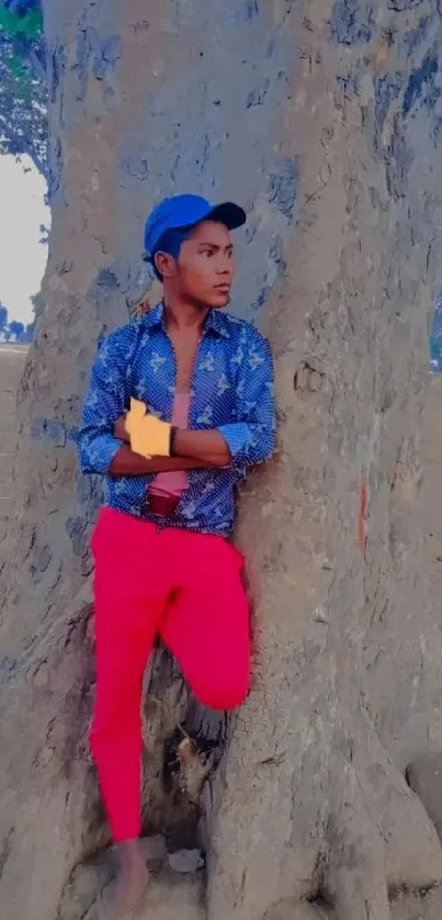 Young man posing by a tree in bright clothes.