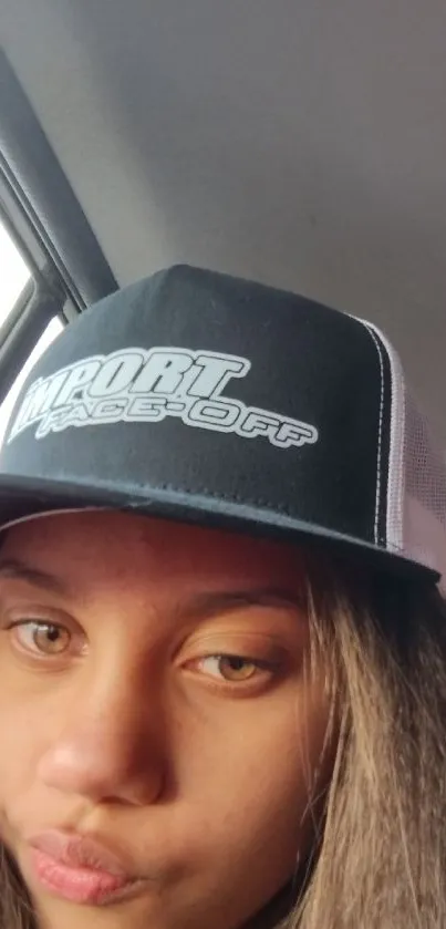 Person in a car wearing a black cap, captured as a mobile wallpaper image.