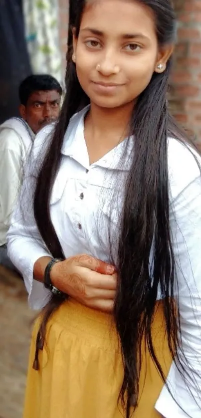 Stylish young woman in casual attire with long hair, posing against a brick wall.