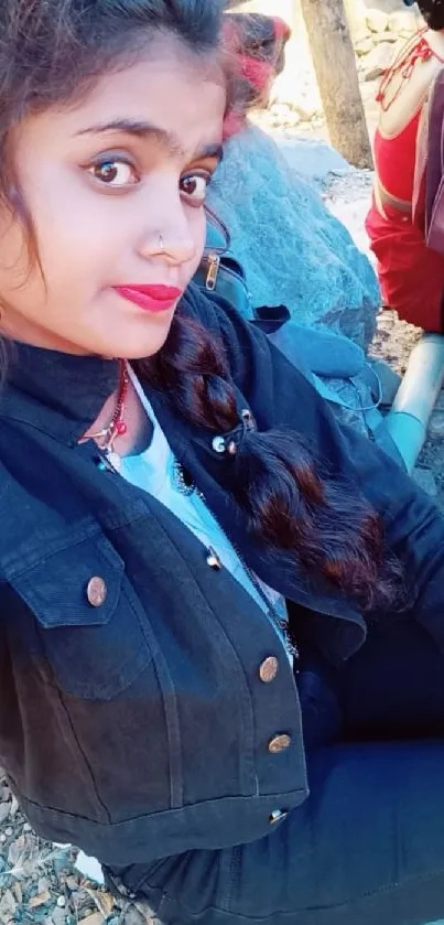 Young woman in denim jacket sitting outdoors.