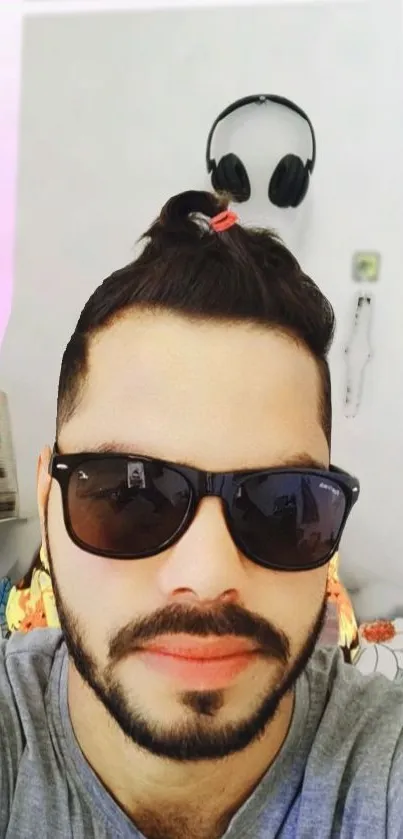 A fashionable man with sunglasses and a man bun, wearing a gray shirt.