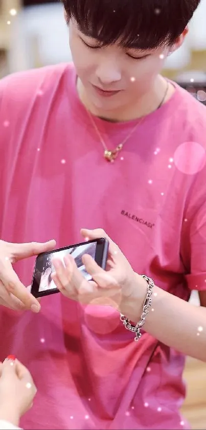 Man in pink shirt showing phone, stylish wallpaper.