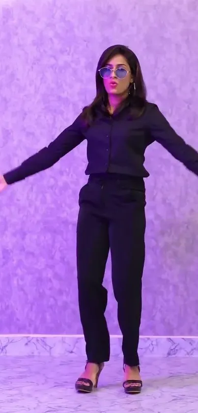 A woman in stylish black attire poses on a purple textured wall.