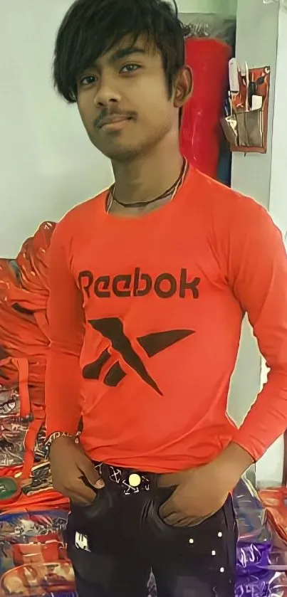 Person in red Reebok shirt and black jeans standing.