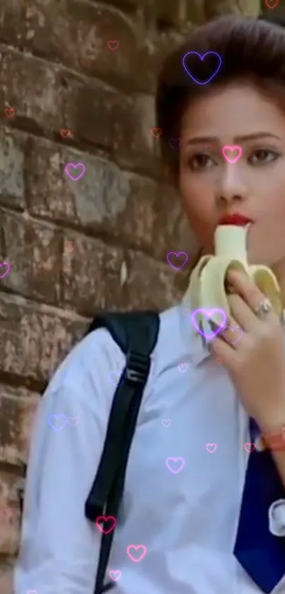 Fashionable schoolgirl eating banana with heart accents on brick wall.