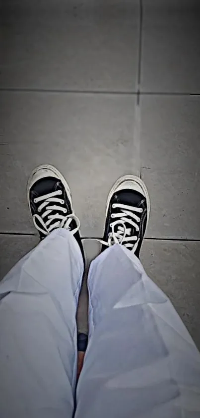 Black sneakers on light gray tiled floor, top view.