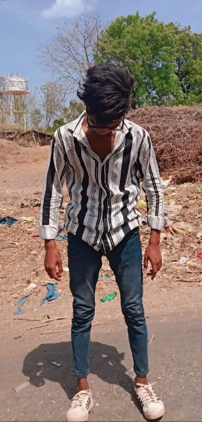 Person in striped shirt standing outdoors with natural background.