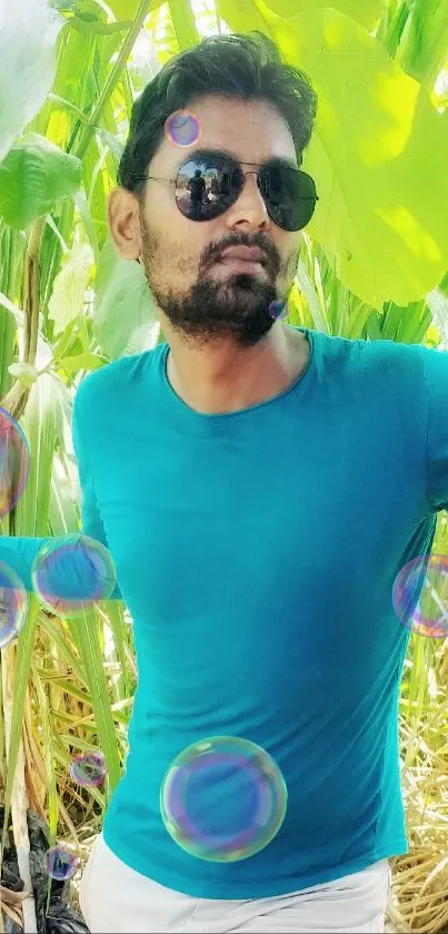 A man in sunglasses with a teal shirt amidst lush green leaves.