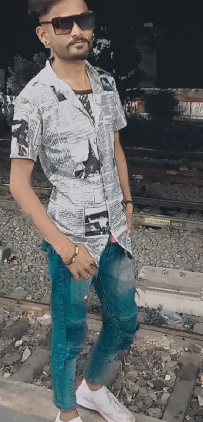 Man in urban outfit stands on railroad track at night.