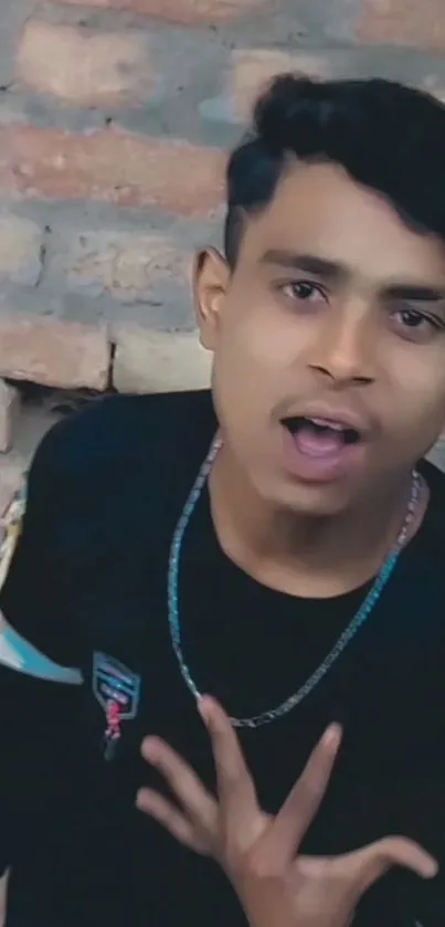 Young man in black against a brick wall, exuding urban style.