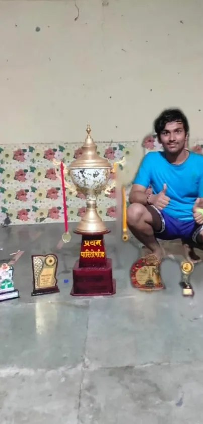 Man kneeling beside a variety of trophies on display.