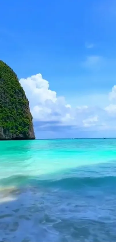 Tropical beach with clear turquoise water and lush green cliffs.